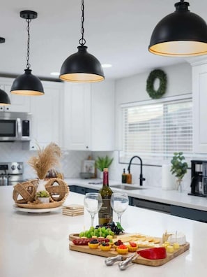 Una cocina con iluminación colgante, una botella de vino y una bandeja de frutas.