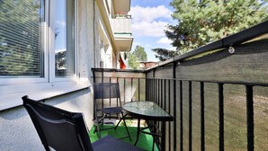 A balcony with a table and chairs, a window, and a view of trees and buildings. - Spacious Apartment | 2 Balconies | Close to the Beach (Gdańsk)