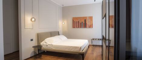 A modern bedroom with a bed, a small side table, and a wall-mounted light fixture.