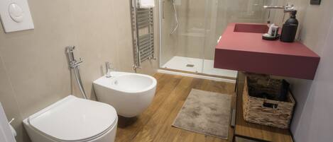 Un baño moderno con bidé, cabina de ducha, tocador con espejo y suelo de madera.