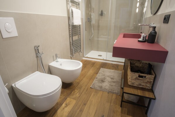 A modern bathroom with a bidet, a shower enclosure, a vanity with a mirror, and a wooden floor.