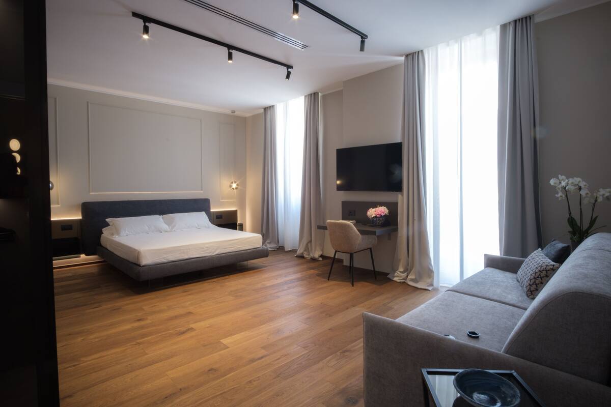 A modern hotel room with a large bed, a sofa, a desk, and a TV.