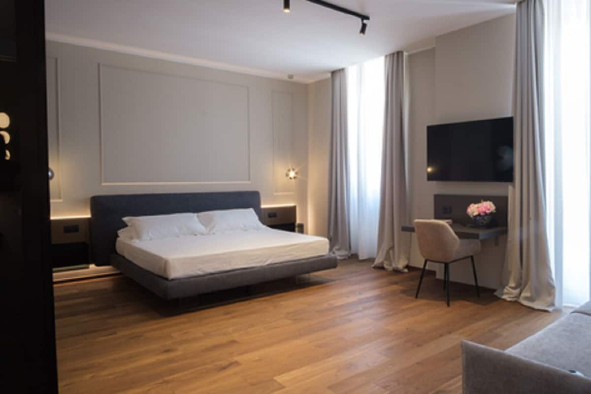 A modern hotel room with a large bed, a desk, a TV, and a sofa.