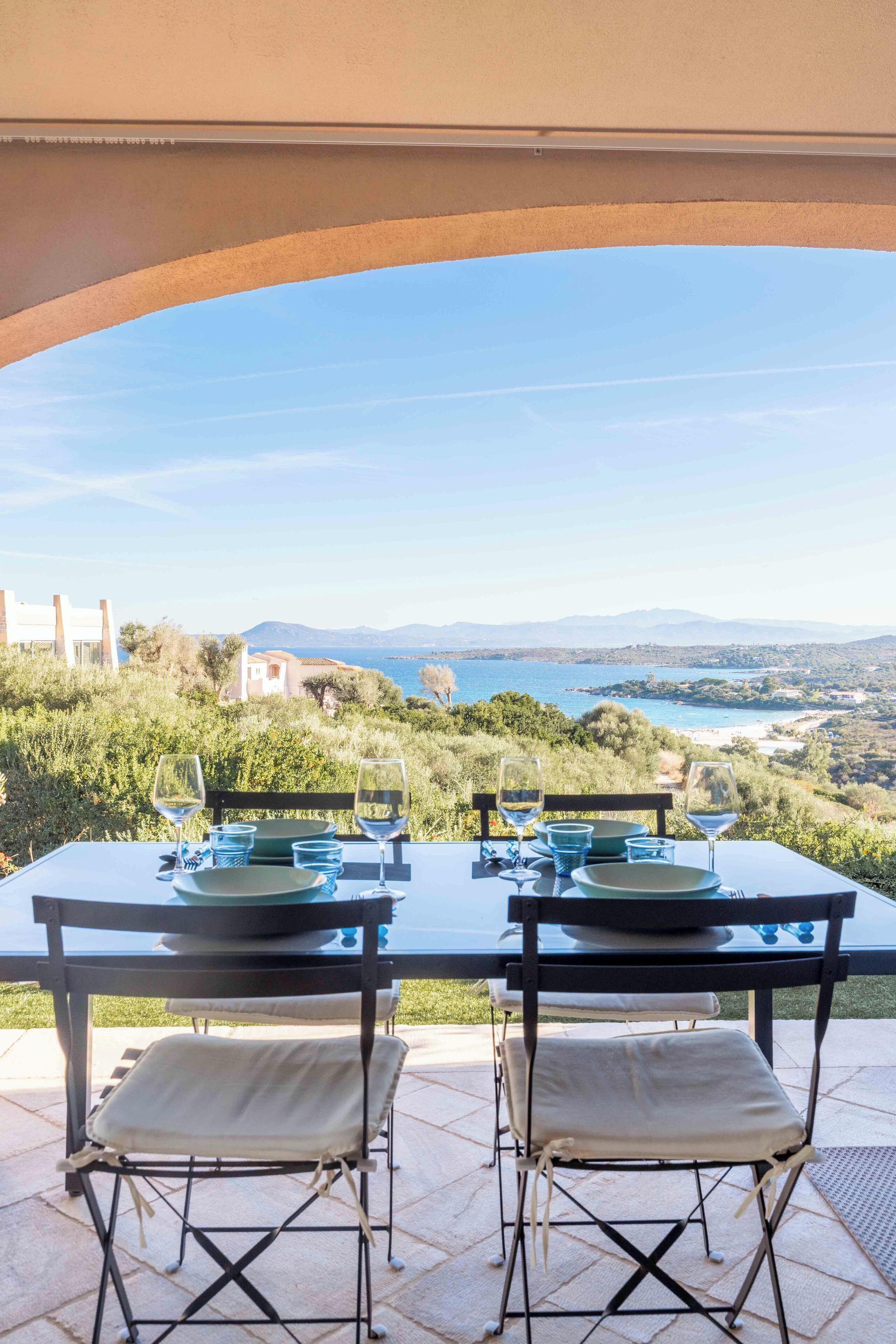 An outdoor dining table with two chairs, set for two, overlooking a scenic coastal landscape.
