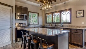 Una cocina moderna con una isla grande, taburetes de bar, electrodomésticos de acero inoxidable y ventanas amplias.