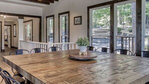 Un comedor amplio con una gran mesa de madera, rodeado de sillas y ventanas grandes que ofrecen vistas al exterior.