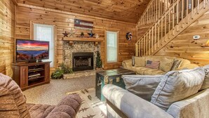 A cozy cabin interior with a fireplace, a television, and a staircase. - Old Glory - WIFI, Hot Tub, Game Room, Free Attraction Tickets!!! (Sevierville)