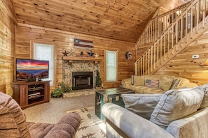 A cozy cabin interior with a fireplace, a television, and a staircase. - Old Glory - WIFI, Hot Tub, Game Room, Free Attraction Tickets!!! (Sevierville)
