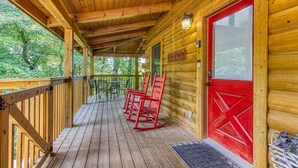 A wooden cabin with a porch, red rocking chairs, and a red door. - Old Glory - WIFI, Hot Tub, Game Room, Free Attraction Tickets!!! (Sevierville)