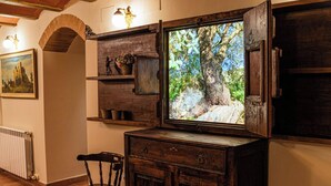 Habitació rústica amb un gran quadre encapçalat d'un arbre, prestatges de fusta, una cadira i un radiador.