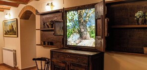A rustic room with a large framed picture of a tree, wooden shelves, a chair, and a radiator. - 8 Bedroom Cottage in Santa Maria de Dulcis (Santa Maria de Dulcis)