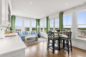 A spacious living area with a sofa, a dining table with chairs, and large windows with curtains.