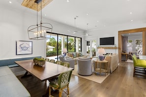 A spacious living area with a wooden dining table, comfortable seating, and large windows offering a view of the outdoors.
