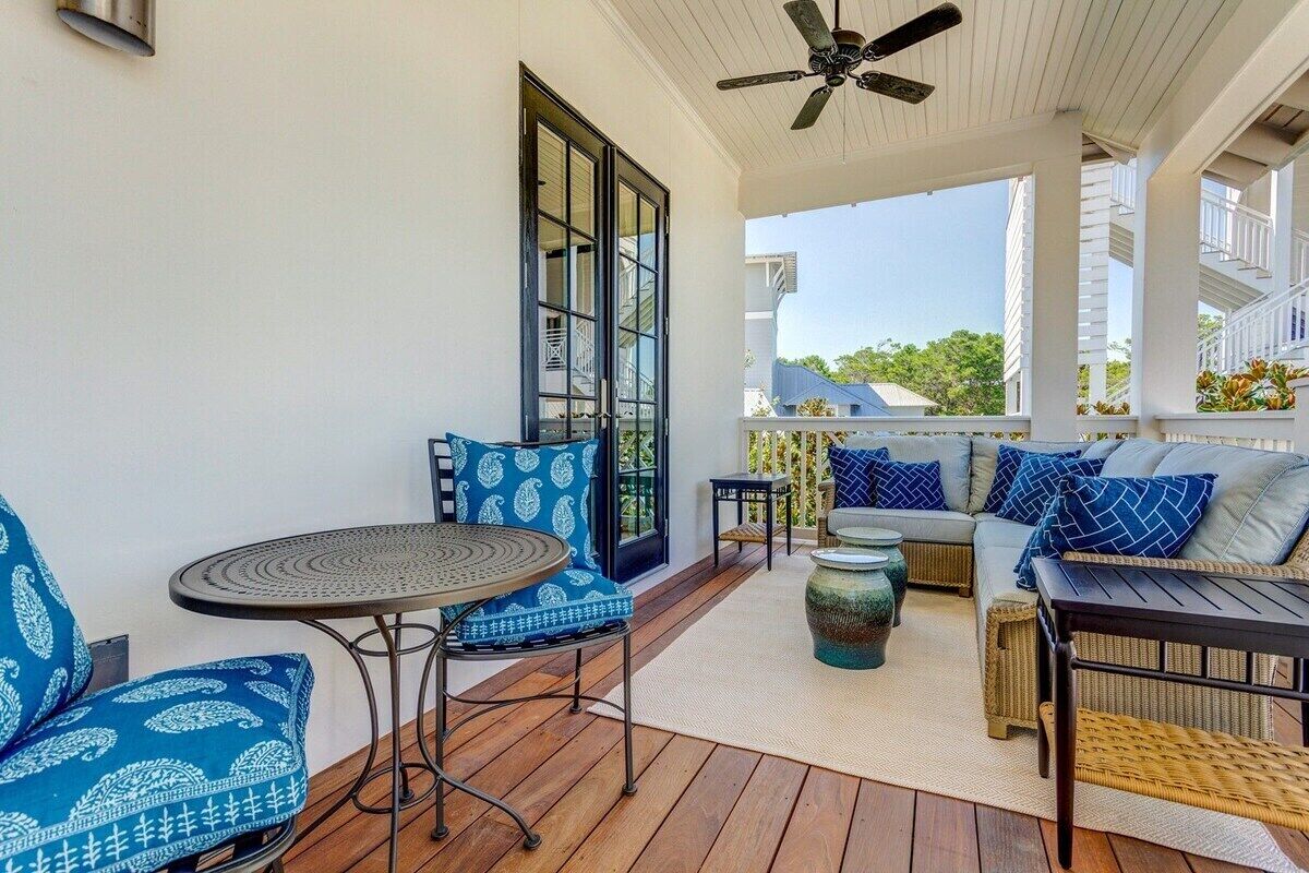 A covered outdoor seating area with a ceiling fan, a round table, and a sofa with patterned cushions.