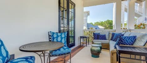 A covered outdoor seating area with a ceiling fan, a round table, and a sofa with patterned cushions.