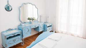 Quarto com cama, cômoda com espelho e uma mesinha com um vaso de flores.