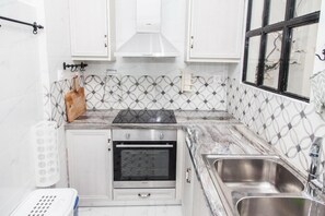 A compact kitchen with white cabinets, a built-in oven, a stainless steel sink, and a patterned backsplash. - Charming Apartment in Pagkrati-GTD95602 (Athens)