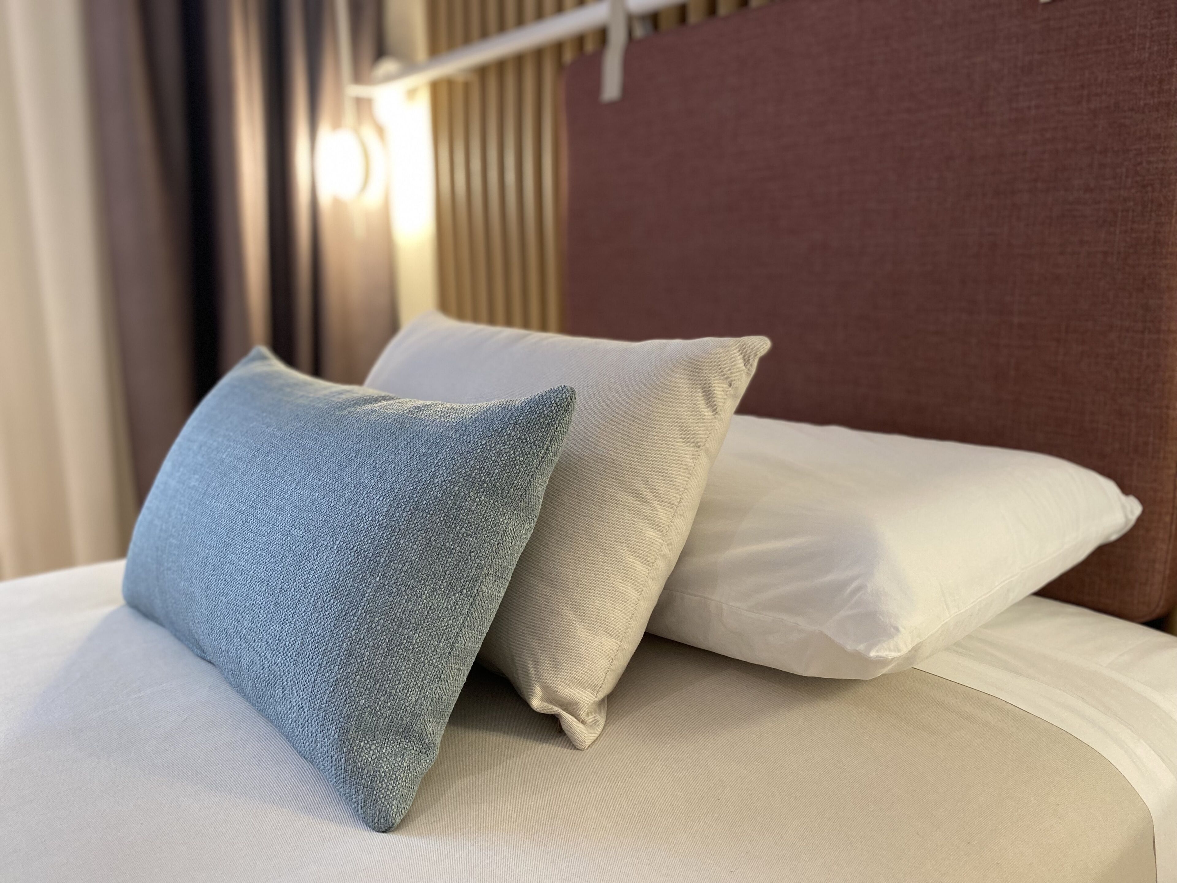 A bed with two pillows, one light blue and one white, in a hotel room.