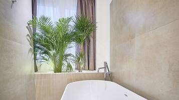 Ein modernes Badezimmer mit einer freistehenden Badewanne, einem Fenster mit Vorhängen und Zimmerpflanzen.