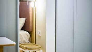 A room with a bed, a small table, and a mirror reflecting the bed and a light fixture.