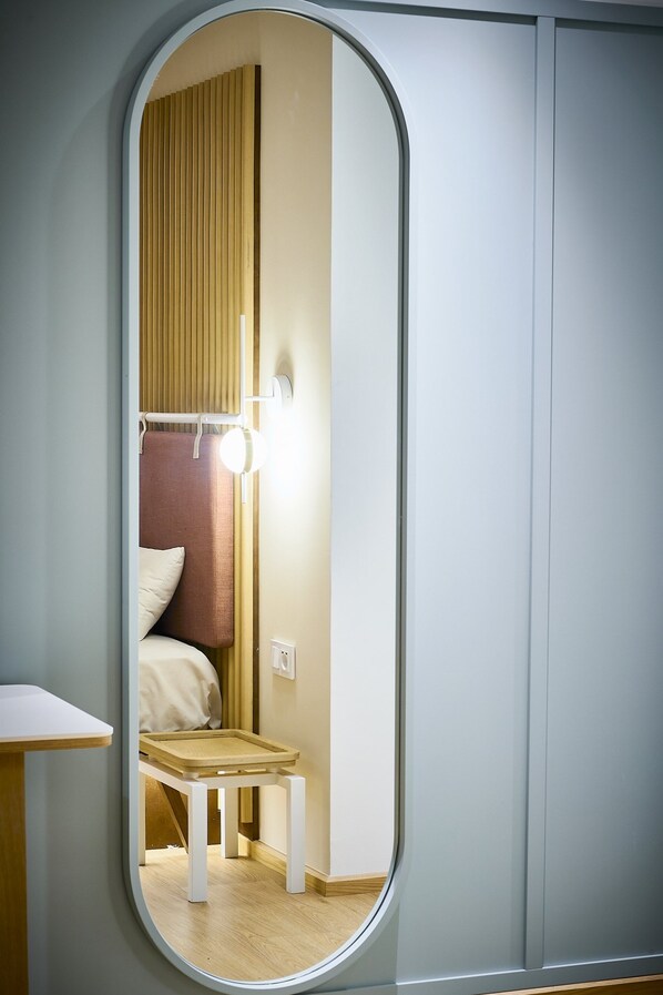 A room with a bed, a small table, and a mirror reflecting the bed and a light fixture. - Hotel Leonor (Conil de la Frontera)