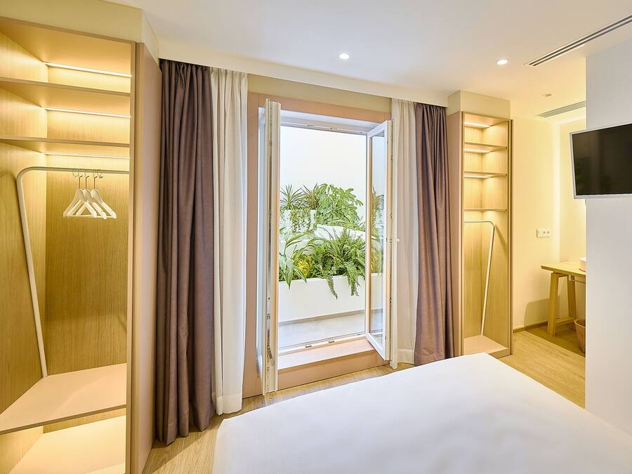 A hotel room with a bed, a TV, a desk, and a view of greenery outside.