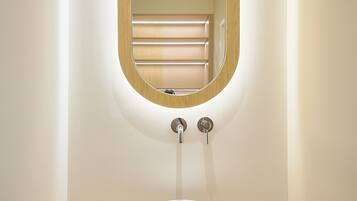 A bathroom with a round white sink, a wooden-framed mirror, and a light fixture above the mirror.