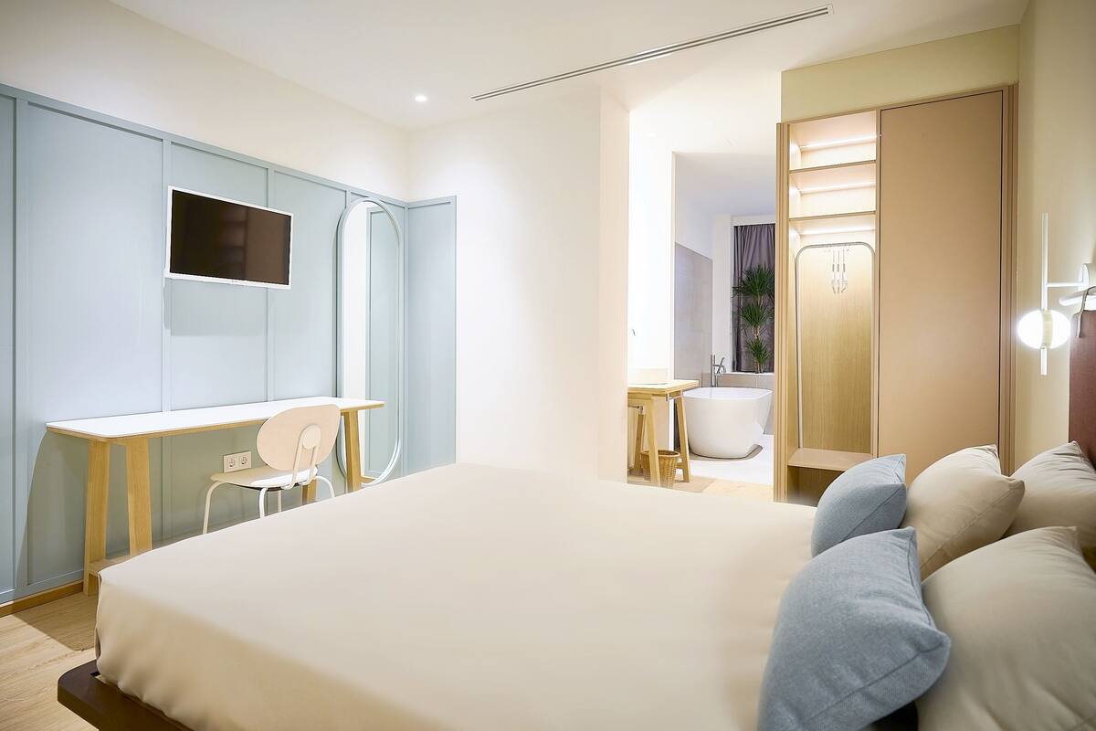 A modern bedroom with a large bed, a desk, a chair, and a wardrobe.