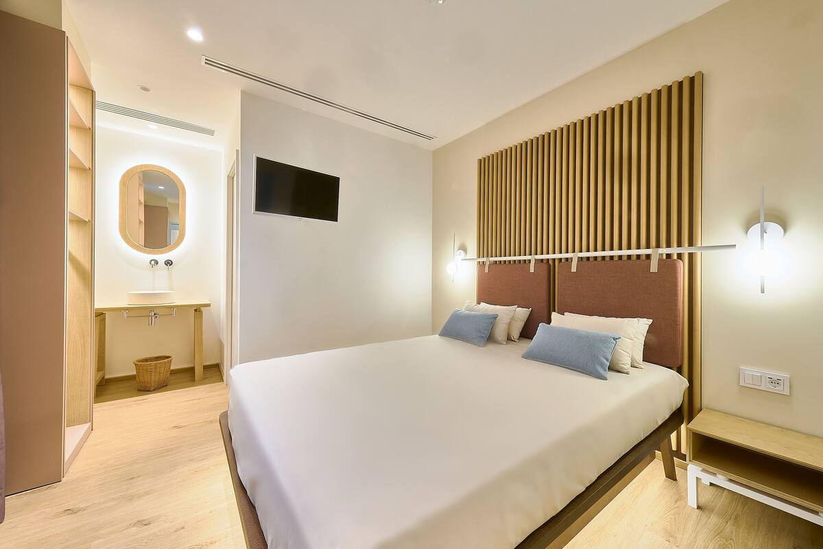 A modern hotel room with a large bed, a bedside table, a wall-mounted TV, and a wooden panel wall design.