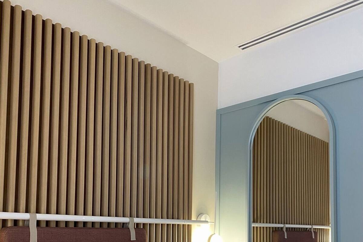 A hotel room with a bed, a headboard, a mirror, and a wall-mounted light fixture.