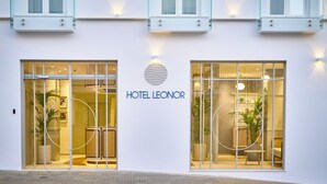 The exterior of Hotel Leonor with large glass windows, a minimalist facade, and a circular logo above the entrance. - Hotel Leonor (Conil de la Frontera)