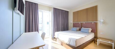 Una habitación de hotel con una cama, un escritorio y un televisor fijado a la pared.