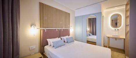 A modern hotel room with a large bed, bedside table, and a mirror with a light.