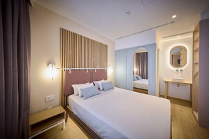 A modern hotel room with a large bed, bedside table, and a mirror with a light.