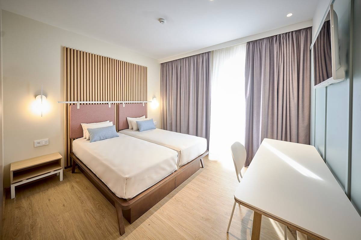 A modern hotel room with two beds, a desk, and a TV.