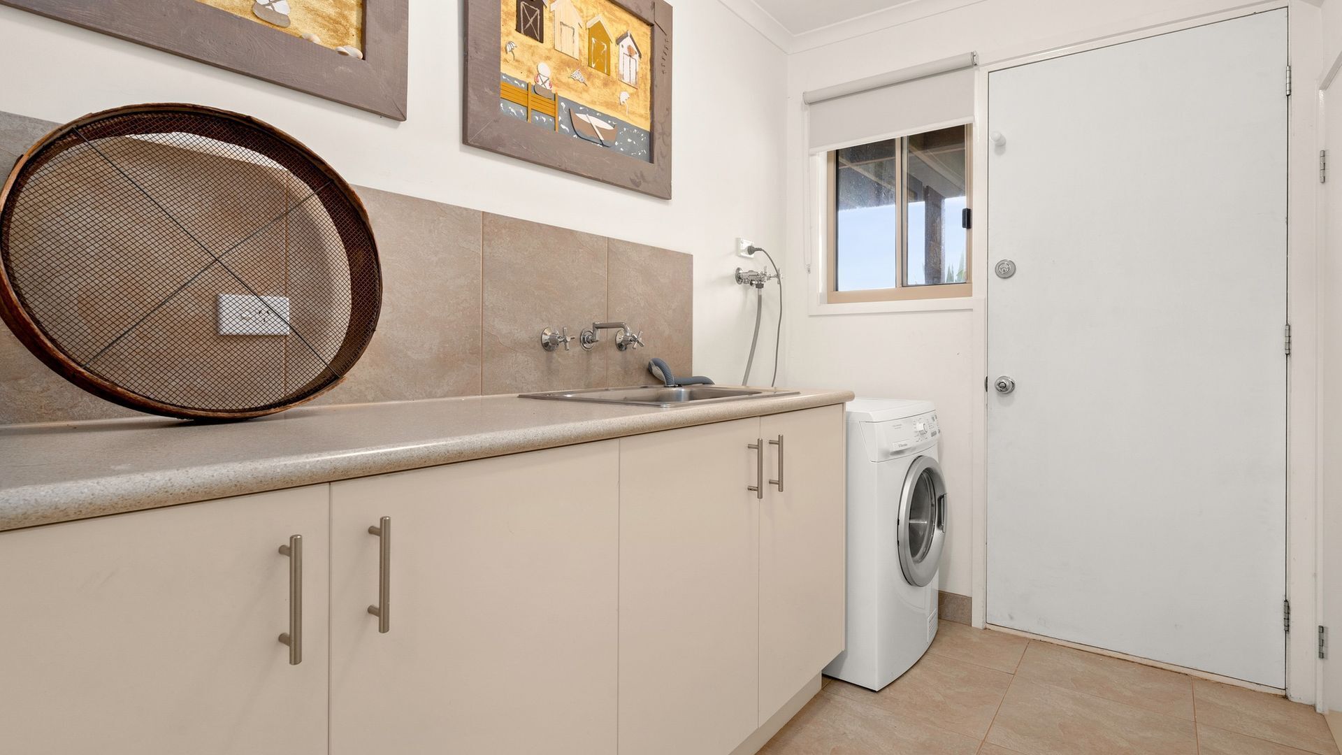 A compact kitchen with a sink, a washing machine, and a large mirror.