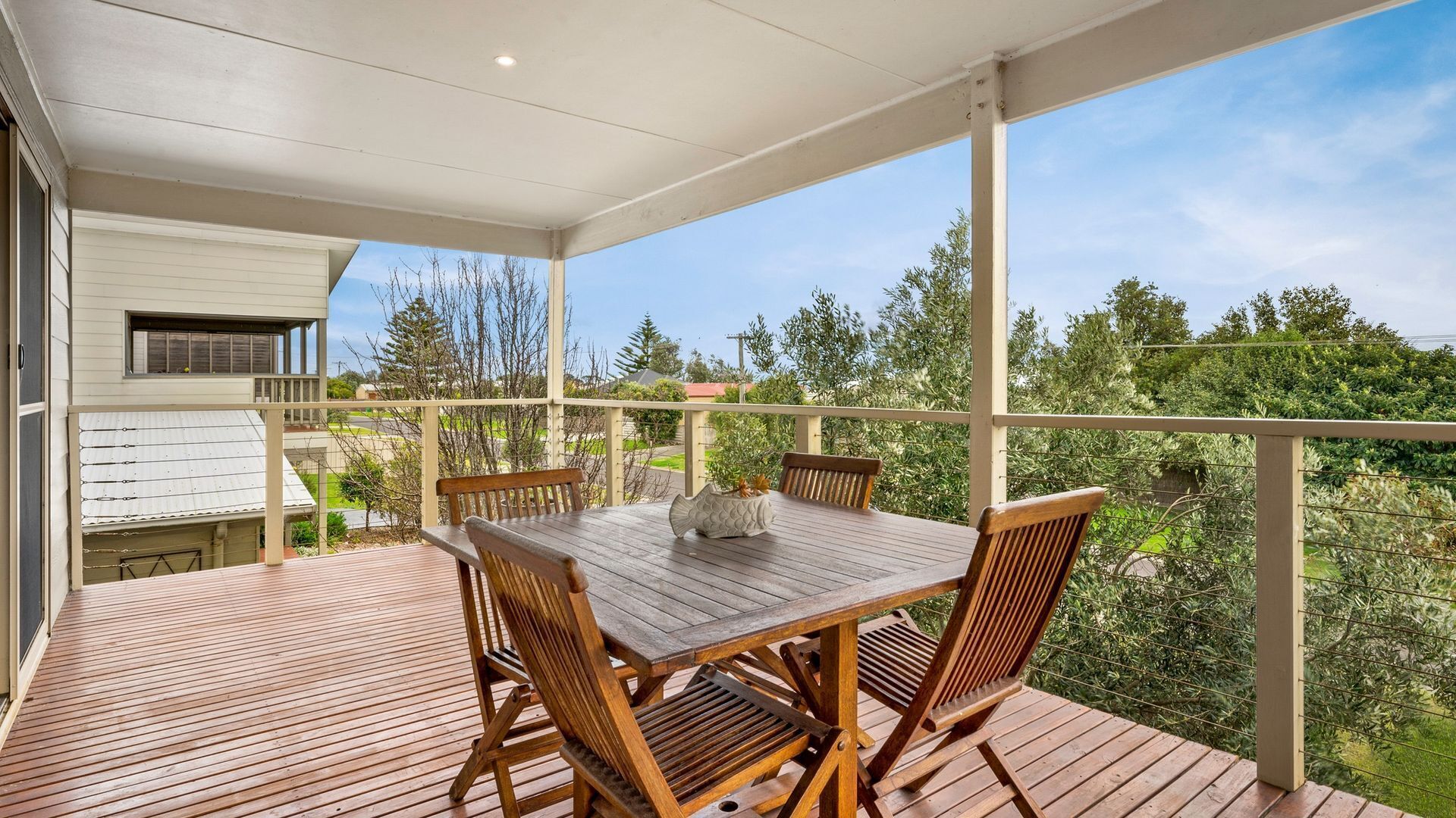 A wooden deck with a table and chairs, overlooking a garden and a residential area.