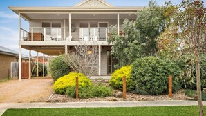 A two-story house with a balcony, a covered porch, and a well-maintained garden with various shrubs and a small tree.