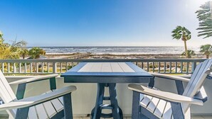 Een balkon met een tafel en stoelen, met uitzicht op het strand.