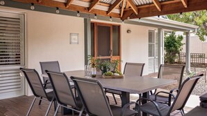 A covered patio with a wooden table and chairs, a bottle of wine, and a fruit basket. - GORGEOUS & WELCOMING COASTAL COTTAGE CLOSE TO TOWN (Dunsborough)