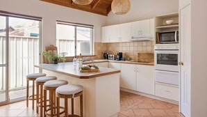 A modern kitchen with white cabinets, a wooden ceiling, and a large island with stools. - GORGEOUS & WELCOMING COASTAL COTTAGE CLOSE TO TOWN (Dunsborough)