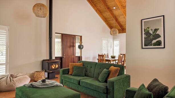 A cozy living room with a green sofa, a wooden ceiling, a fireplace, and a dining area. - GORGEOUS & WELCOMING COASTAL COTTAGE CLOSE TO TOWN (Dunsborough)