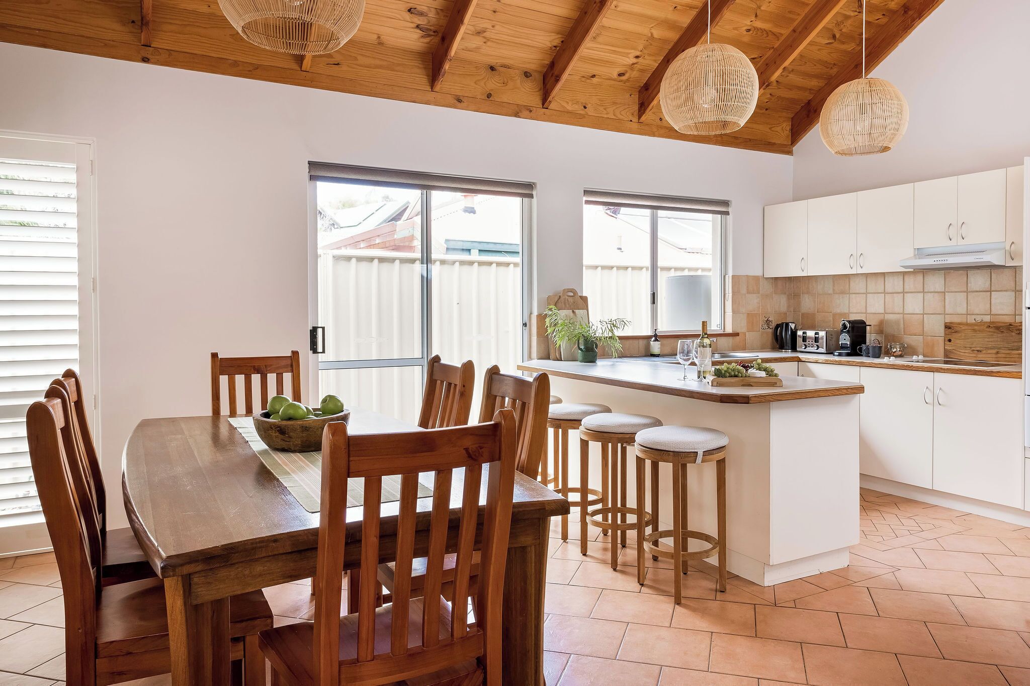 A modern kitchen with white cabinets, a wooden dining table, and a bar area.