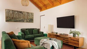 A living room with a green sofa set, a wooden cabinet, a flat-screen TV, and a large forest-themed painting. - GORGEOUS & WELCOMING COASTAL COTTAGE CLOSE TO TOWN (Dunsborough)