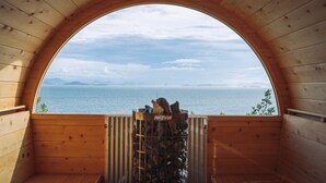 Una cabaña de madera con un amplio ventanal arqueado que da a un cuerpo de agua y tierra distante.