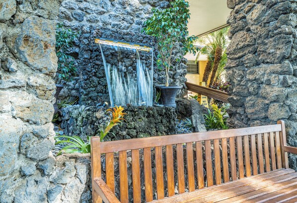 Un muro de piedra con una cascada y un banco de madera.