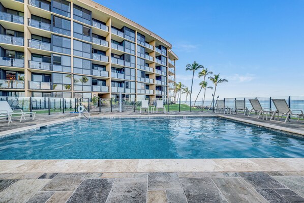A hotel with a pool, palm trees, and a view of the ocean. - Unwind and Immerse Yourself in Stunning Ocean Views with AC- Kihei Surfside #305 (Kihei, Maui)
