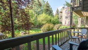Une terrasse en bois avec des meubles d’extérieur, une fontaine en pierre et un jardin bien entretenu, agrémenté d’arbres et d’arbustes.