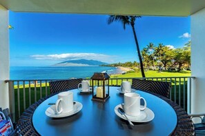 Ein Tisch mit weißen Tassen und Untertellern, einer Kerze und Blick auf das Meer und die Berge.