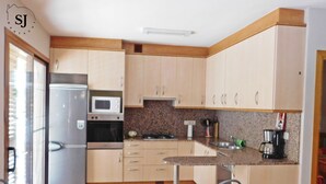 Une cuisine avec des meubles de rangement en bois clair, un réfrigérateur en acier inoxydable, un four à micro-ondes et une machine à café.